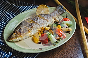 Grilled white fish on a dish on a table in a restaurant with a glass of white wine.