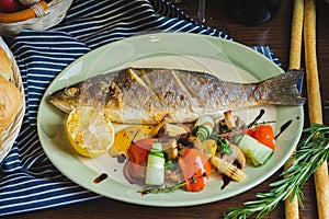 Grilled white fish on a dish on a table in a restaurant with a glass of white wine.