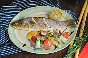 Grilled white fish on a dish on a table in a restaurant with a glass of white wine.