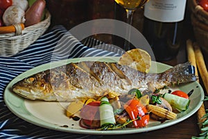 Grilled white fish on a dish on a table in a restaurant with a glass of white wine.