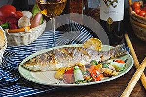 Grilled white fish on a dish on a table in a restaurant with a glass of white wine.