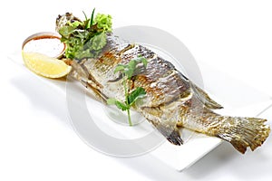 Grilled Whole Barramundi Fish Pra-Kra-Pong with Red Chili Garlic Seafood Sauce and a piece of lemon on white porcelain plate, photo