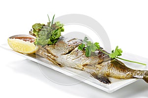 Grilled Whole Barramundi Fish with Red Chili Garlic Seafood Sauce and a piece of lemon on white porcelain plate, isolated on white
