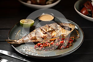 Grilled whole dorado fish served with vegetables, sauce and lemon on a blue plate. Seafood food