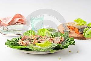 Grilled wild salmon and lettuce dish with green pesto, linen, cutlery, plate, glass of water on white background