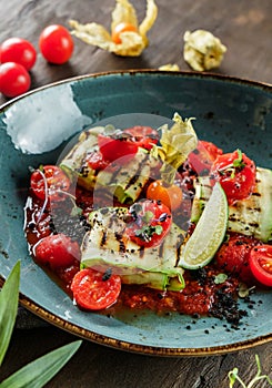 Grilled zucchini with cherry tomatoes and sauce in plate on wooden background. Healthy vegan food, clean eating, dieting, close up
