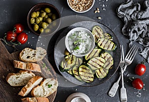 Grilled zucchini, olives, tomatoes, ciabatta - simple snack or appetizer. Mediterranean style food. On a dark background, top view