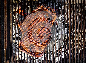 Grilling marinated beef flank steak on hot coals barbecue grill