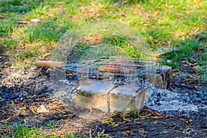 Grilling sausages in portable barbecue grill on campfire