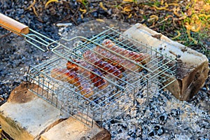 Grilling sausages in portable barbecue grill on campfire