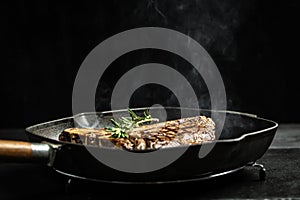 Grilling a tasty tender marinated t-bone steak seasoned with fresh rosemary on frying grill pan on black. wagyu porterhouse