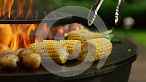 Grilling vegetables cooking on fire outside. Man hands turning corn with forceps