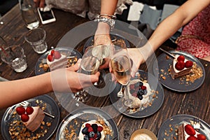 Grils party. Grils cheers glasses with champagne in restraunt. Dessert cakes background