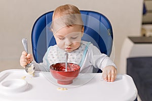 The grimy infant or toddler tries to eat independently. Baby-led weaning. Little child eats himself with a spoon.