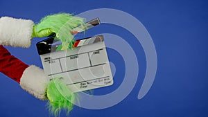 The Grinch's green haired hand holds a movie clapper on an isolated blue background. Gift kidnapper cosplay photo