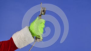 The Grinch's green haired hand holds out an antique telephone receiver on a blue isolated background. Gift Snatcher