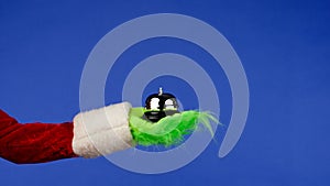 Grinch's green haired hand holds reception bell on an isolated blue background. Gift kidnapper cosplay. Christmas photo