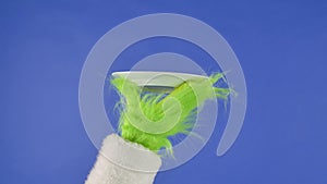 The Grinch's green haired hand shows a white plate on an isolated blue background. Gift snatcher cosplay. Christmas