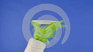 The Grinch's green haired hand shows a white plate on an isolated blue background. Gift snatcher cosplay. Christmas