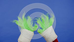 The Grinchs green haired hands against an isolated blue background. Gift kidnapper cosplay. Christmas and New Year photo