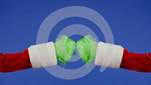 Grinch's green hairy hands touching fists on blue isolated background. Gift snatcher cosplay. Christmas and new year