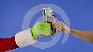 The Grinchs green haired hand hold a Christmas sock with dollar bills and a mans hand takes it away. Gift