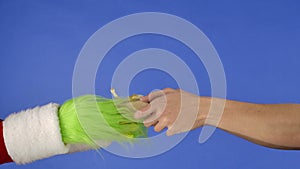 Grinchs green haired hand hold a gift box and a mans hand takes it away on a blue isolated background. Gift