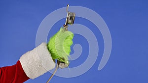 The Grinchs green haired hand holds an antique telephone receiver on a blue isolated background. Gift Snatcher