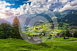 Grindelwald village view and summer Swiss Alps mountains panorama landscape, wooden chalets on green fields and high peaks in