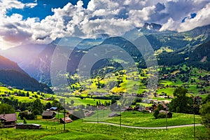 Grindelwald village view and summer Swiss Alps mountains panorama landscape, wooden chalets on green fields and high peaks in