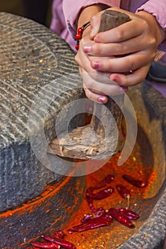 Grinding the chilli peppers into powder traditional way turning the mill by hand