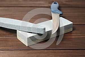 Grindstones. Two whetstones and steel knife blade. Oval and rectangular double layer sharpening stone on wooden table background