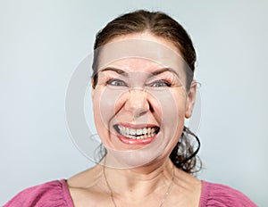 Grinning adult woman with teeth, angry and annoyed person, portrait on grey background, emotions series