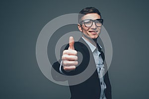 Grinning man in dark suit jacket with two thumbs up over gray background. Includes copy space.