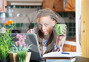 Grinning woman in kitchen with homework and laptop