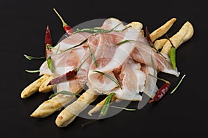 Grissini bread sticks with prosciutto on a wooden board with red and green pepper