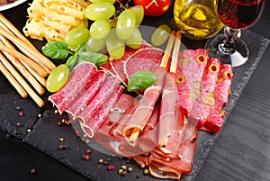 Grissini stick bread with ham on black board with appetizers