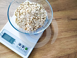 Grits weighing in glass bowl on the kitchen scales on wooden table.