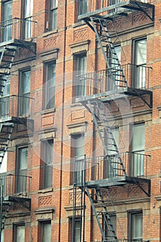 Gritty exterior of orange brick  tenement style apartment building with black fire escapes in central Manhattan, New York City