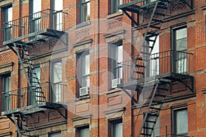 Gritty exterior of orange brick  tenement style apartment building with black fire escapes in central Manhattan, New York City