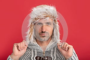 grizzled guy face in sweater and earflap hat on red background, face