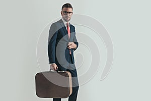 Grizzled hair man in his forties buttoning suit and holding luggage