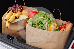 Groceries from a supermarket in a car trunk. Food delivery during quarantine. Cruft Paper eco bags for shopping. Fresh