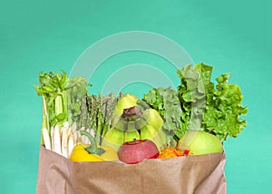 Grocery bag of produce, fruits and veggies on green background