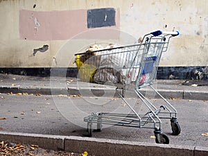 A grocery cart filled with package of potatoes against a shabby wall.