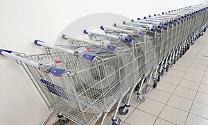 Grocery carts in a row against a white wall. Parking of grocery carts