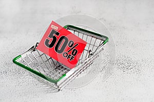 Grocery mini shopping basket with red card with fifty percent discount sign. Conceptual image of clearance sale, seasonal