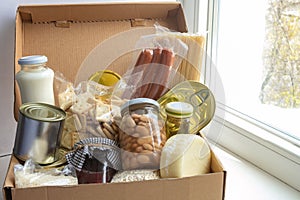 Grocery set for needy in crisis, pasta, beans, canned food etc in cardboard box on the windowsill, food donation concept