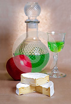 Grocery still life of cheese with mold, apple, glasses and absinthe in a decanter