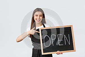 Grocery store employees, small business and coffee shops concept. Cheerful cute female barista in black apron pointing